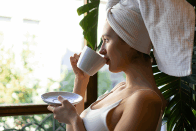 A woman with a towel on her head drinking from a mug as part of her morning routine for anxiety.
